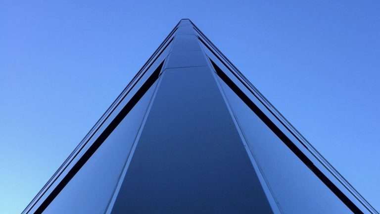 The edge of a glass tower rising to a point against a clear blue sky